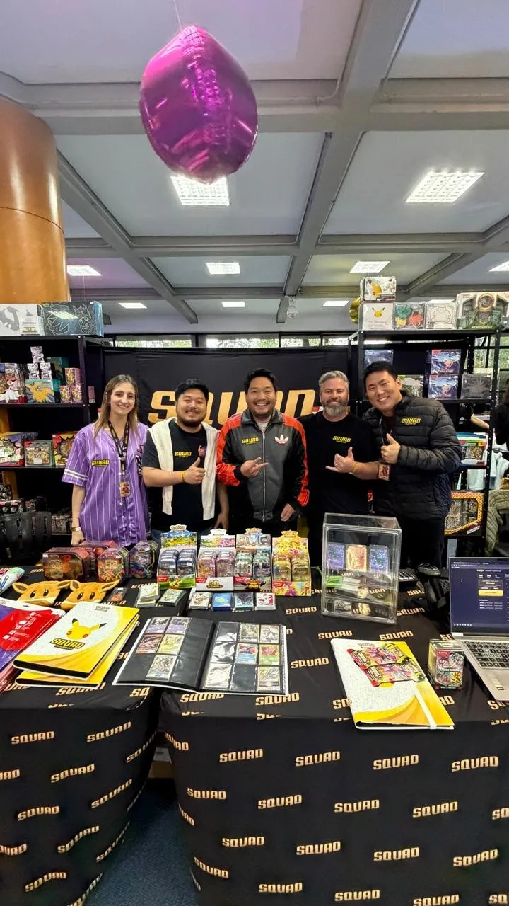 Equipe da Squad no estande, com produtos de Pokémon TCG na mesa